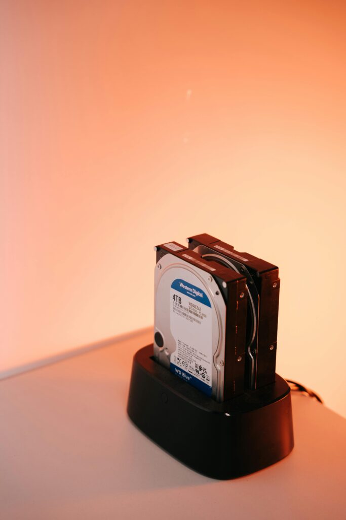 Dual external hard drives on a docking station with an orange backdrop.