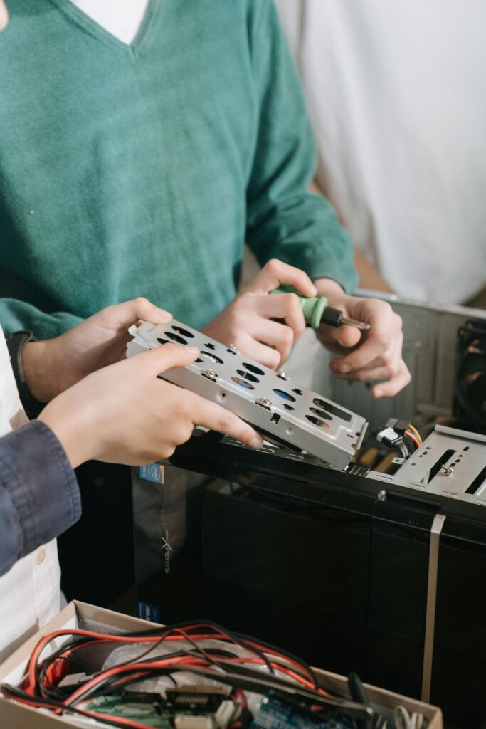 Close-up of technicians repairing computer hardware with tools, focusing on hands and equipment.